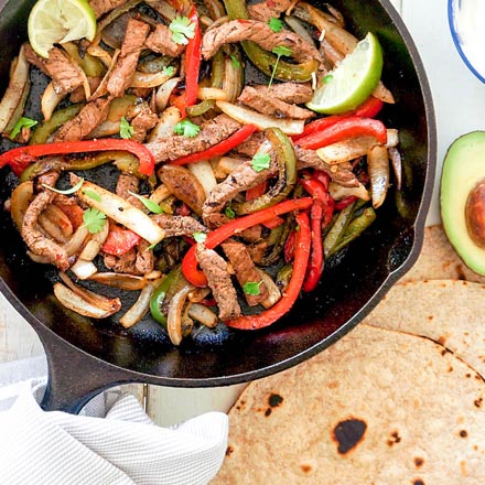 Sizzling beef fajitas with colorful bell peppers and onions being served on a steaming cast iron skillet