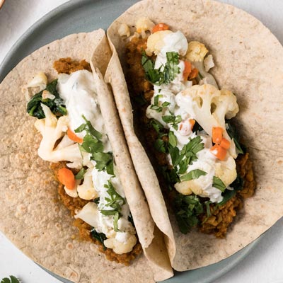 Curried lentil wrap with roasted vegetables and yogurt sauce dripping from the sides