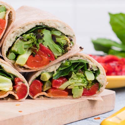 Mediterranean wrap cut diagonally, displaying roasted broccoli and red peppers with white bean spread