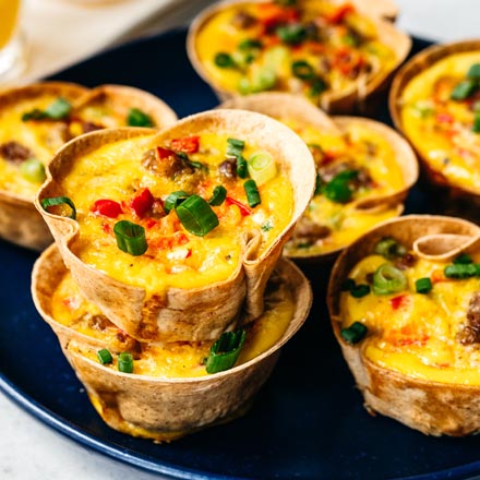 Golden-brown breakfast cups in a muffin tin, with eggs and sausage visible in crispy tortilla shells