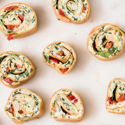 Spiral arranged spinach artichoke roll-ups showing cream cheese swirls with red peppers