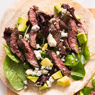 Sliced steak wrap revealing medium-rare skirt steak, blue cheese crumbles, and fresh avocado